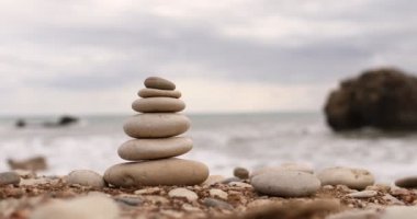 Mavi deniz arka planında güneşli bir günde deniz kıyısındaki piramit taşları. İyi tatiller. Kızın eli bir piramit inşa ediyor. Çakıl taşı plajı, sakin deniz, seyahat yeri. Denizde mutlu tatil kavramı