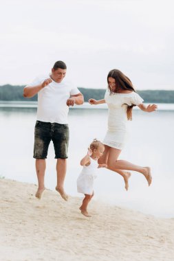 Mutlu genç bir aile göl kenarında eğleniyor, anne baba ve kız açık havada oynuyorlar. Yaz tatili, anneler, babalar günü, bebekler günü. Birlikte vakit geçirmek. Aile görünüşü