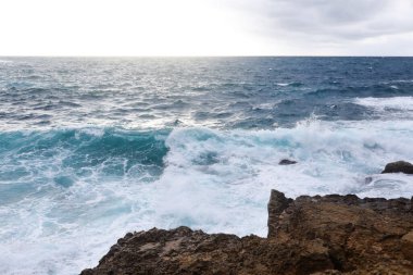 Kıbrıs 'ta bir plajda kayalık kayalıklara vuran dalgalar su sporları için tehlikeli olabilir ama aynı zamanda dalgalar ve sıçramaları güzel ve vahşi.