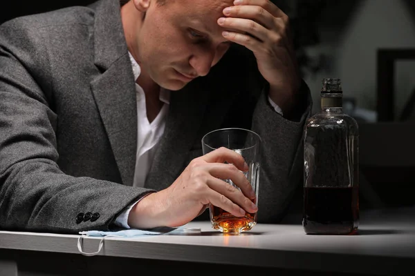 A man with bottle of whiskey on the kitchen. The concept of drunkenness and alcoholism. Alcoholic father. A tired sick man in sorrow drinks alone. Emotional experience. selective focus.