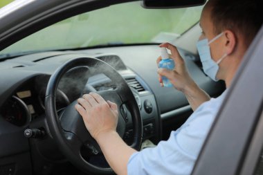 Direksiyon başına antibakteriyel dezenfektan sıkmak, enfeksiyon kontrol konsepti. Coronavirus 'u, COVID-19' u, gribi önle. Tıbbi koruyucu maskeli bir adam araba kullanıyor.