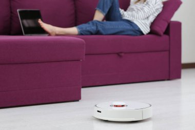 Robot temizleyicisi. Kız evde kanepede dinlenirken robot elektrik süpürgesi çalışıyor. Kendin için konsept zamanı. Akıllı ev. Modern kız zamanını optimize ediyor. Robot konsepti. seçici odak.