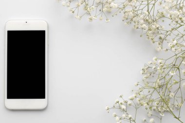 Beyaz arka planda çiçekler olan boş ekranlı üst görüşlü cep telefonu. Fotokopi alanı olan düz çiçek çerçevesi