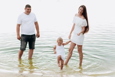 Anne, baba ve kız göl kenarında eğleniyorlar. Yaz tatili kavramı. Anneler günü, babalar günü, bebekler günü. Aile doğada birlikte vakit geçiriyor. Aile görünüşü. Güneş ışığı