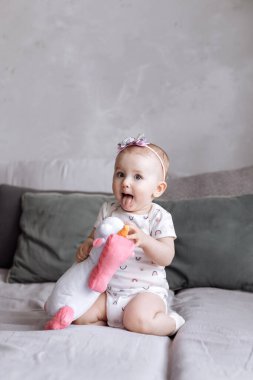 Sevimli küçük kız evde yatakta oyuncak tek boynuzlu atıyla oynuyor. Çocukluk günü konsepti. Mutlu bebekler, aile günü.