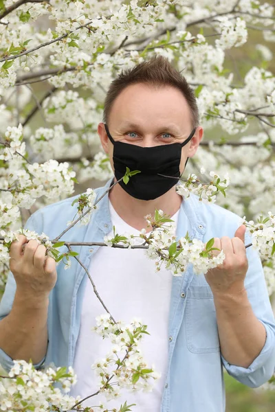 man in mask among flowering trees. man in a medical mask among a blossoming spring garden. Self-isolation and quarantine. cheerful man rejoices in the end of the pandemic and enjoys the spring