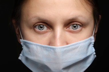 Siyah arka planda tıbbi maske takan genç bir kadının yakın plan portresi. Karantina, koronavirüs salgını, covid-19. Evde kal konsepti. Virüs koruması.