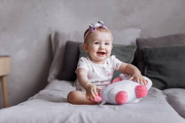Sevimli küçük kız evde yatakta oyuncak tek boynuzlu atıyla oynuyor. Çocukluk günü konsepti. Mutlu bebekler, aile günü