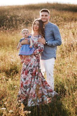 Anne, baba ve küçük kız yaz günü çimlerin üzerinde eğleniyorlar. Anneler, babalar ve bebekler günü. Yürüyüşe çıkan mutlu bir aile