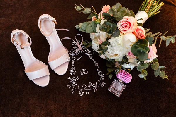 Wedding accessories on the wooden table: a bridal bouquet, wedding rings, white shoes and perfume. wedding morning preparation.