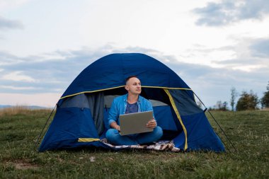 Genç erkek serbest çalışan dağlarda bir dizüstü bilgisayar üzerinde çalışıyor. Serbest konsept.