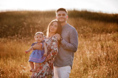 Anne, baba ve küçük kız yaz günü çimlerin üzerinde eğleniyorlar. Anneler, babalar ve bebekler günü. Yürüyüşe çıkan mutlu bir aile.