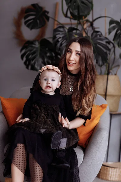 Bela mãe senta-se em uma cadeira e mantém sua filha no colo em casa. conceito de aparência familiar. mães, babys dia . — Fotografia de Stock