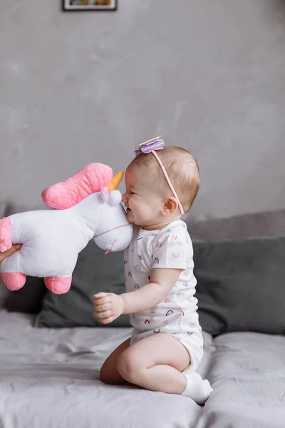 Adorable little girl is playing with toy unicorn on bed at home. concept of childhood day. happy babys, family day — Stock Photo, Image