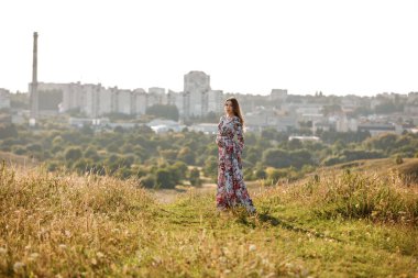 Genç ve güzel bir kadın arka planda çimlerle yaz tarlasında yürüyor..