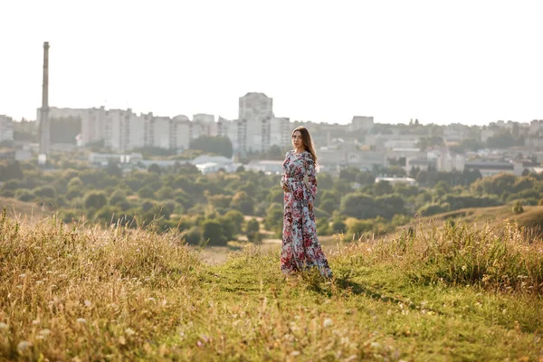 Genç ve güzel bir kadın arka planda çimlerle yaz tarlasında yürüyor..