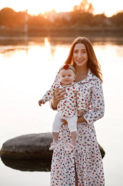 Anne, küçük kızım dışarıda. Genç anne ve küçük kız gün batımında göl kenarında sahilde yürüyorlar. Gölette aile tatili. Doğada çocuklu bir anne portresi. Anneler Günün kutlu olsun..