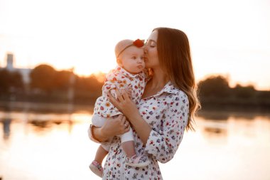 Anne, küçük kızım dışarıda. Genç anne ve küçük kız gün batımında göl kenarında sahilde yürüyorlar. Gölette aile tatili. Doğada çocuklu bir anne portresi. Anneler Günün kutlu olsun..