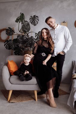 Güzel genç ebeveynlerin portresi ve onların sevimli küçük kızları kameraya bakıyor ve içeride gülümsüyor. Anneler günü, babalar günü, bebekler günü. Aile kavramı. Aile görünüşü.