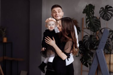 Güzel, genç ebeveynlerin portresi ve onların sevimli küçük kızları kucaklaşmaları, kapalı alanda gülümsemeleri. Anneler günü, babalar günü, bebekler günü. Aile kavramı. Aile görünüşü.