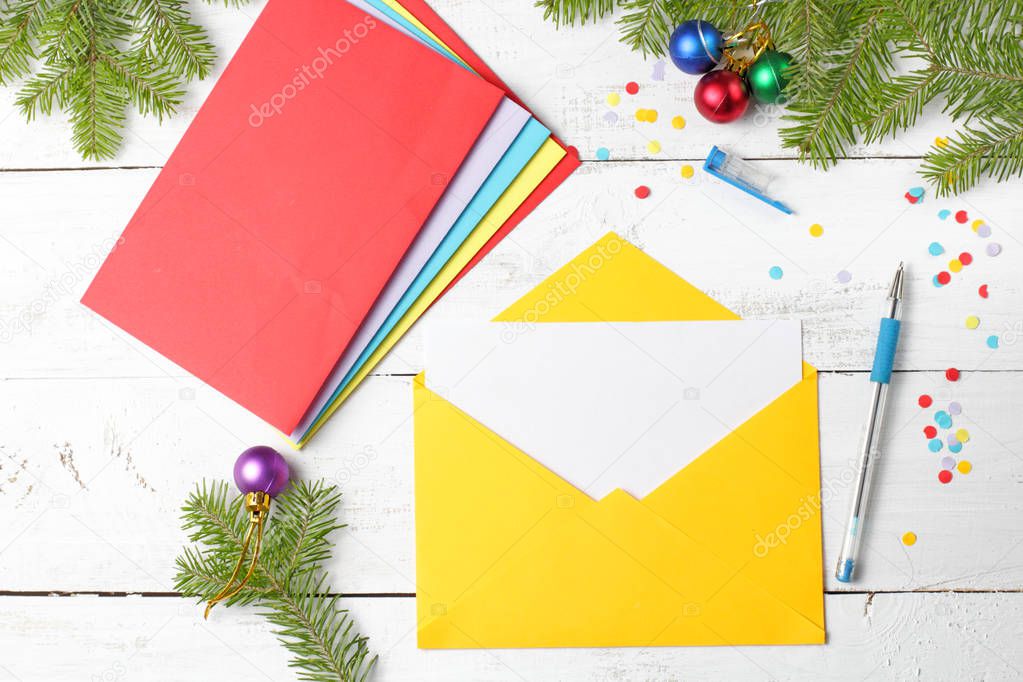 Yellow envelope with blank paper, concept of Christmas greetings or invitations, Christmas tree branches, Christmas balls, confetti.