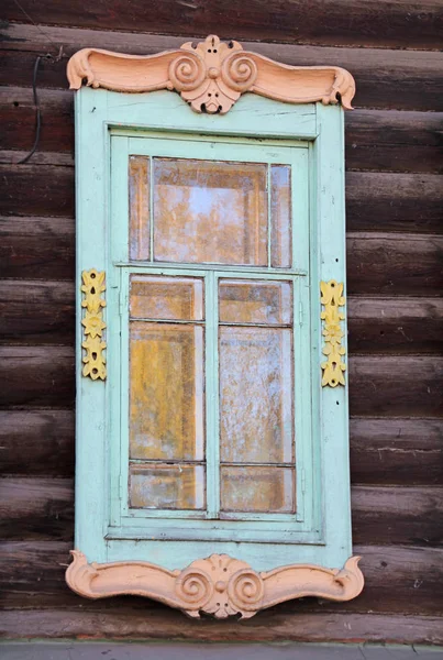 Velha janela esculpida com pintura a cores em uma antiga casa de madeira, close-up . — Fotografia de Stock