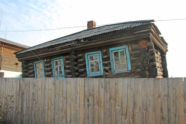 Una vieja casa de troncos detrás de una valla cayó de su lado desde la edad o el tiempo . —  Fotos de Stock