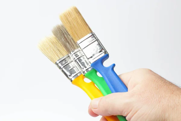 Three paint brushes with colored handle in the right hand of a worker close-up on a white background. — 스톡 사진