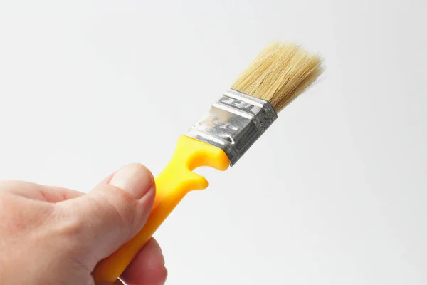 Paint brush with a yellow handle in the left hand of a worker close-up on a white background. — 스톡 사진