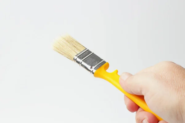 Paint brush with a yellow handle in the hand of a worker, close-up, white background. — 스톡 사진