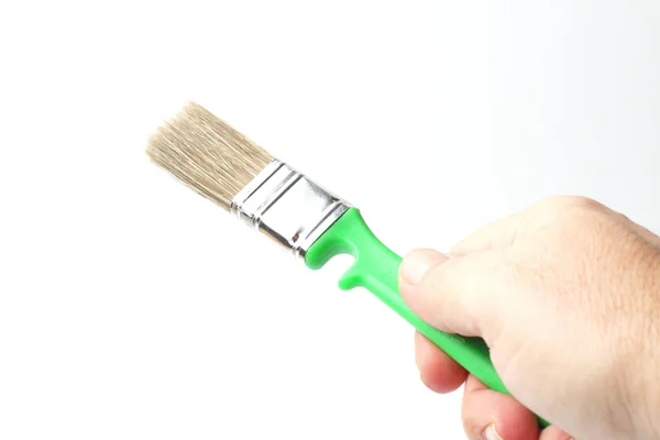 Paint brush with a green handle in the right hand of a worker on a white background, close-up. — 스톡 사진