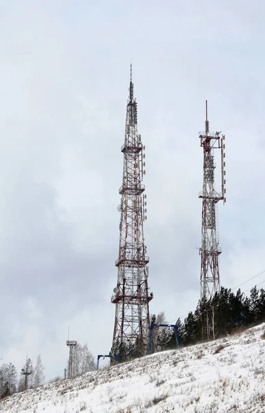 Towers or antennas of cellular communication 4G and 5G or television broadcasting against a cloudy sky on a mountain, winter landscape.
