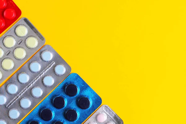 Medical pills in packs on a yellow background close-up, flat lay, copy space.