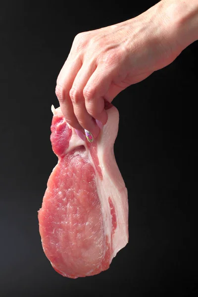 生の豚肉ステーキ 大きな作品は 女性の手を閉じると 黒の背景に — ストック写真