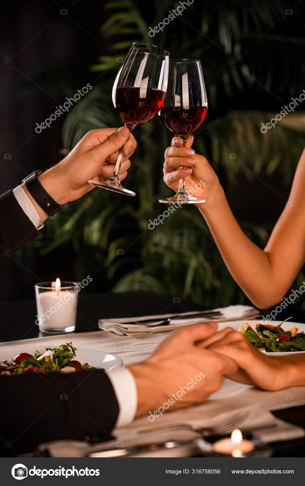 Vertical cropped image of young couple holding hands and wine