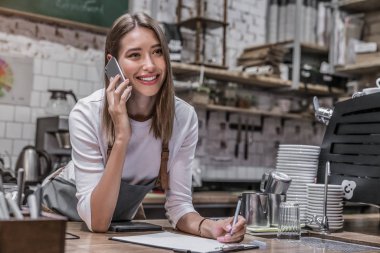 Genç ve mutlu bar sahibi tezgahta akıllı telefonla konuşuyor ve gülümseyerek yüzünü çeviriyor.