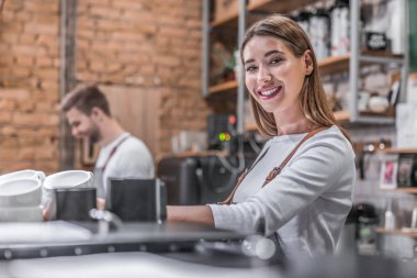 Kafe tezgahının arkasında kahve makinesi kullanarak kahve hazırlayan beyaz bir kadın.