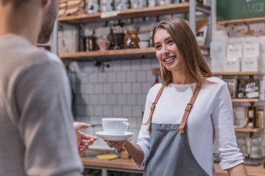 Kahve dükkanında müşteriye hizmet eden neşeli bayan barista.