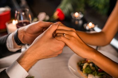 Romantik bir buluşmada şarap ve mumlarla el ele tutuşan çifti kapatın.