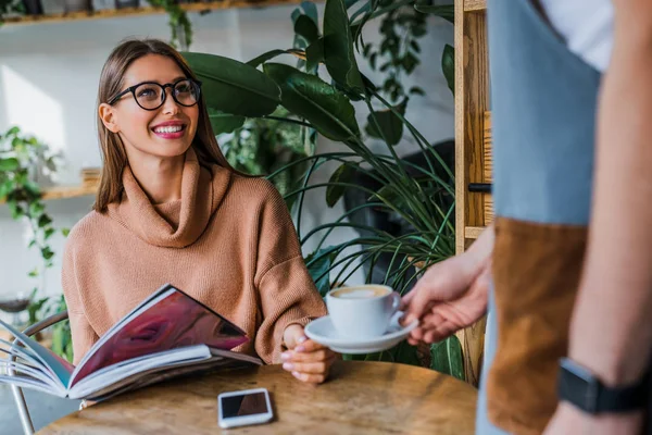 Ober serveert kopje koffie aan lachende blanke vrouw klant in cafetaria — Stockfoto