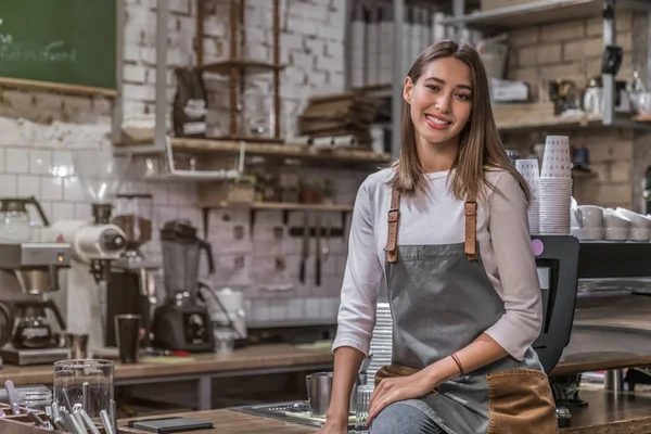 Vrouwelijke coffeeshop eigenaar zittend op de toonbank en glimlachend in camera — Stockfoto
