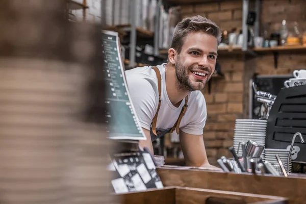 Indoor shot of happy young bar owner standing at the counter and looking away smiling — Stock Photo, Image