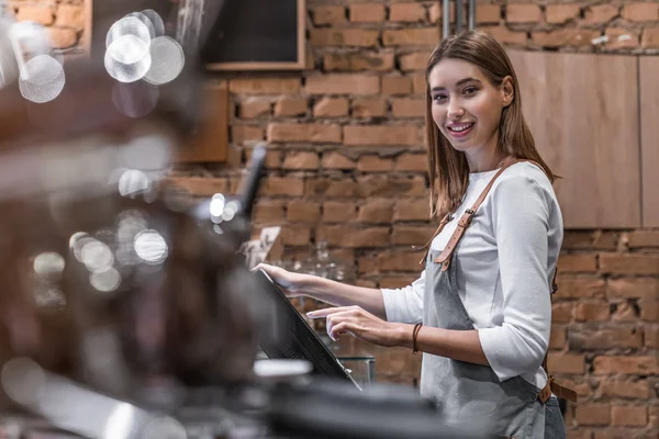 Portret van een vrolijke jonge vrouw aan de balie met een kassa in de coffeeshop — Stockfoto