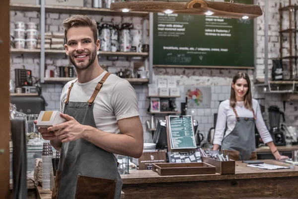 Small business owner working at his coffee shop with female barista on the background — Stock Photo, Image