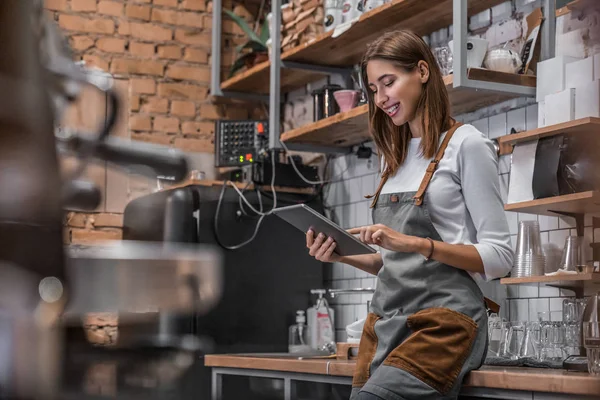 Mosolygós kávézó tulajdonosa áll a munkahelyén, közel a pulthoz, és a digitális tabletta — Stock Fotó