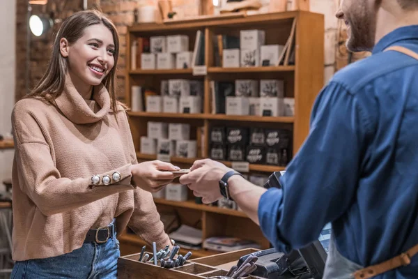 Barista áll a pult mögött egy kávézóban, hitelkártyát vesz el a női ügyféltől, hogy fizessen a vásárlásáért. — Stock Fotó