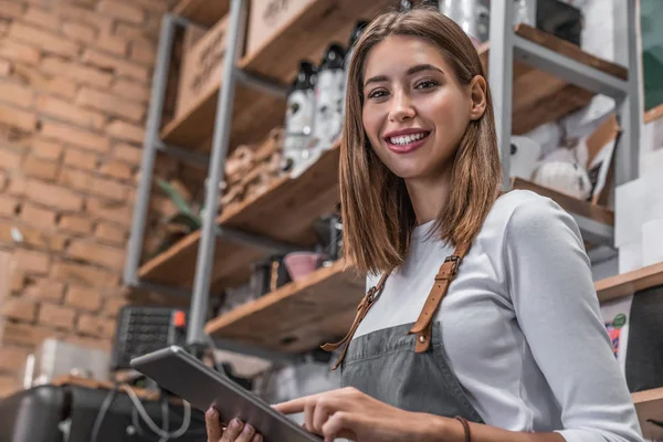 Portret van een lachende koffiewinkeleigenaar die in haar winkel staat en digitale tablet gebruikt — Stockfoto