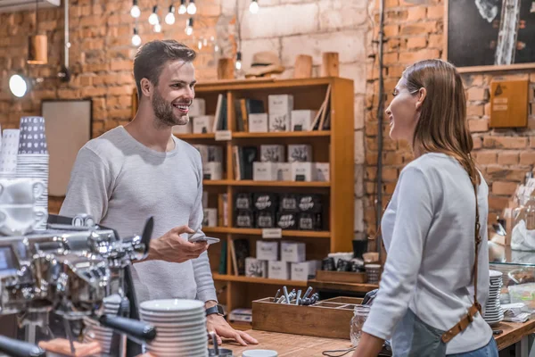 Coffee shop female owner at the counter accepting order from customer with smartphone in hand — Stock Photo, Image
