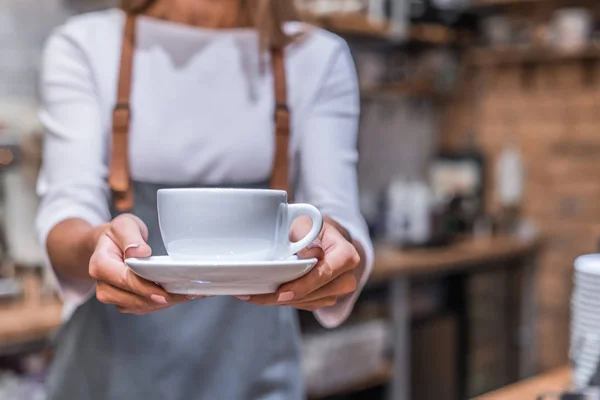 Jonge vrouw barista houden koffie kopje serveren klant in coffeeshop — Stockfoto