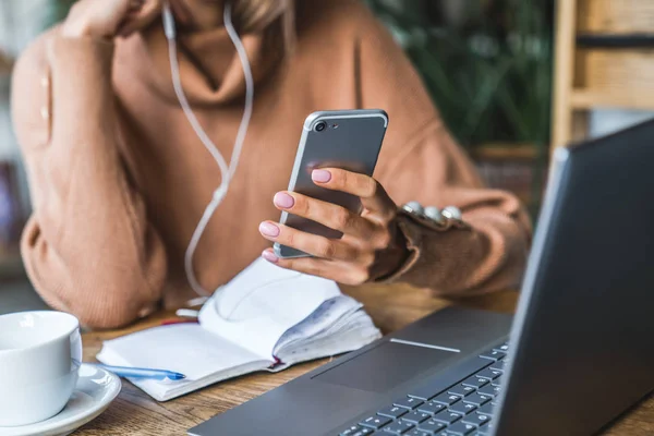 Primo piano colpo di smartphone utilizzato da una donna in auricolare seduto a tavola — Foto Stock